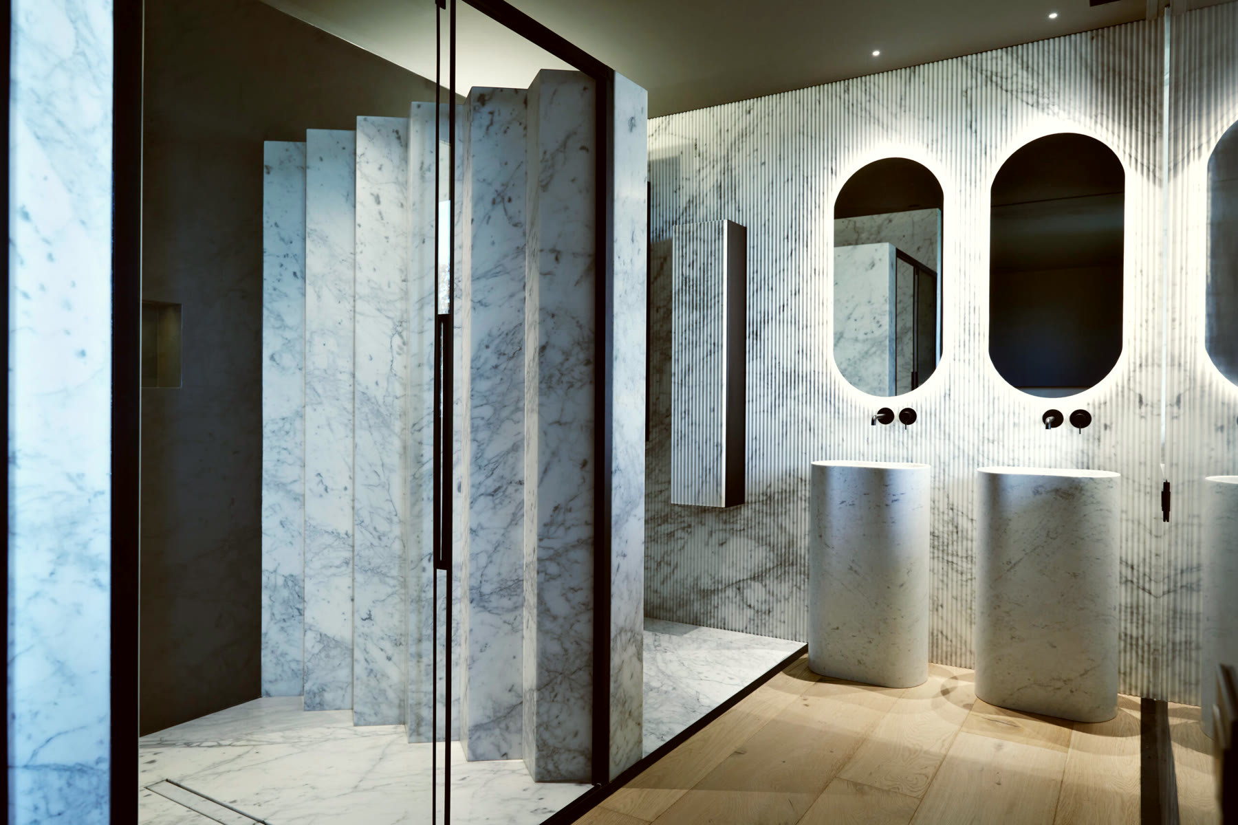 Bagno in marmo di Carrara con doppio lavabo a colonna e specchi ad arco retroilluminati